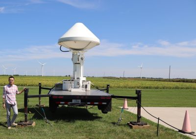 Researcher standing next to X-Band doppler radar and thermal cameras deployed in an Iowa wind farm