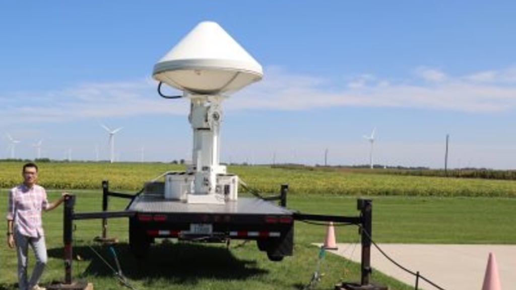 Researcher standing next to X-Band doppler radar and thermal cameras deployed in an Iowa wind farm